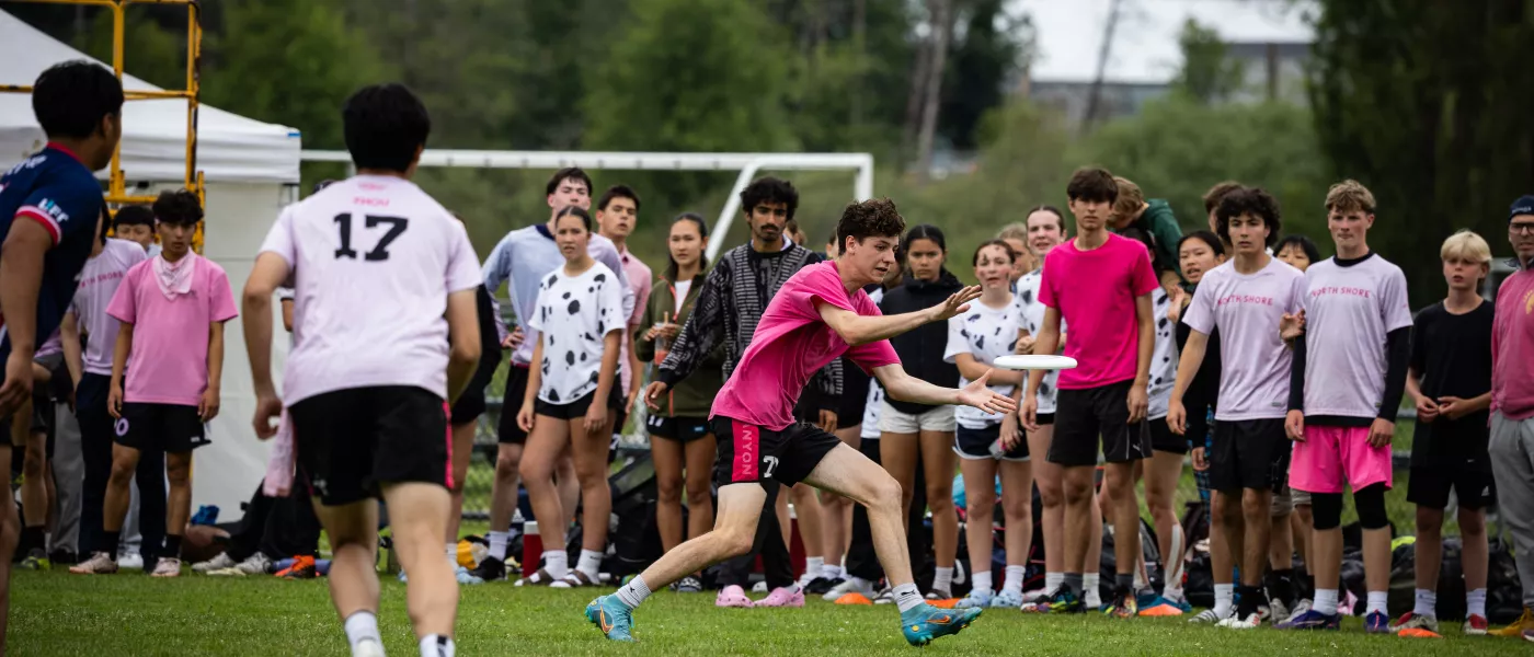 A youth player catching a disc, with a large crowd behind.
